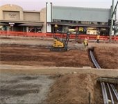 Contruction of Grand Avenue showing small excavator working in the road. 